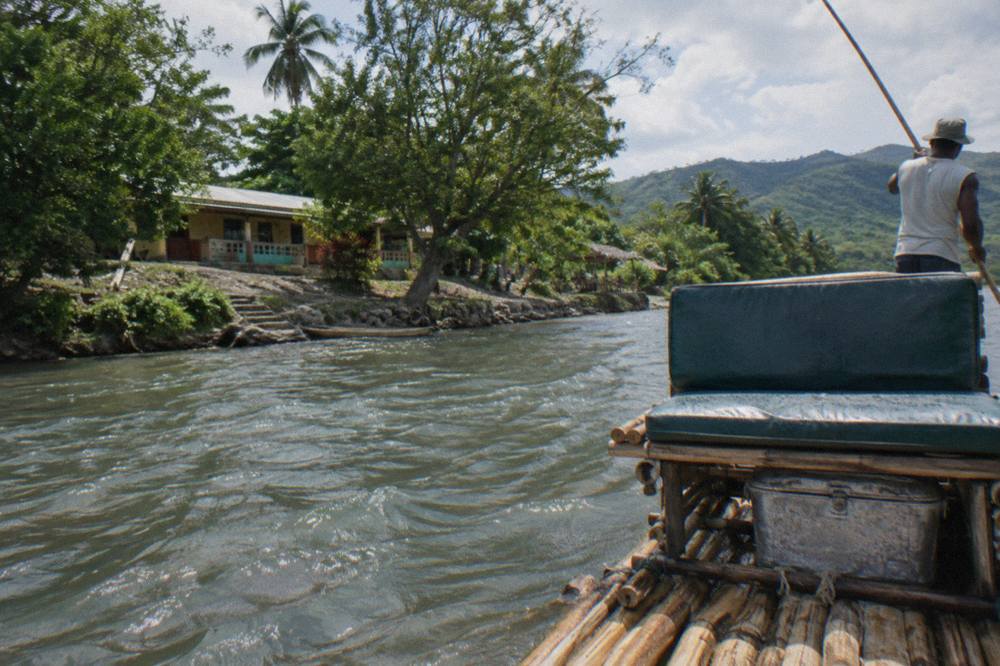 Two empty padded seats on the front of a long bamboo raft moored at a riverbank