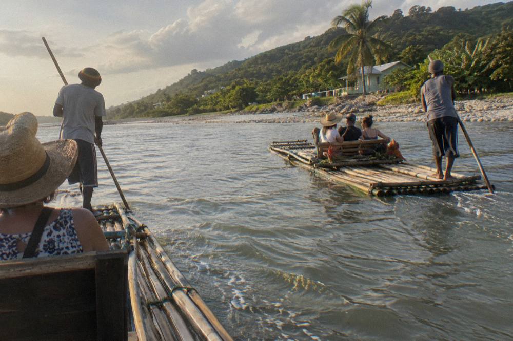 Two bamboo rafts floating side by side on a wide calm river between green banks