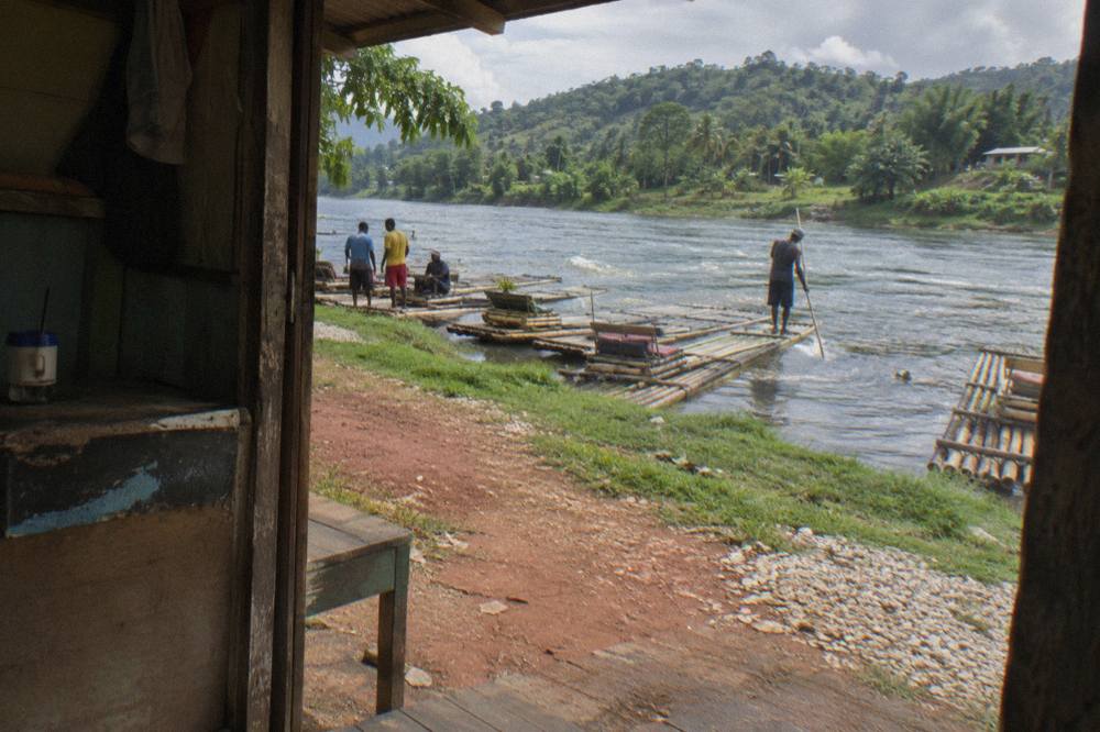 A wide slow green river bend with bamboo rafts moored along a grassy bank