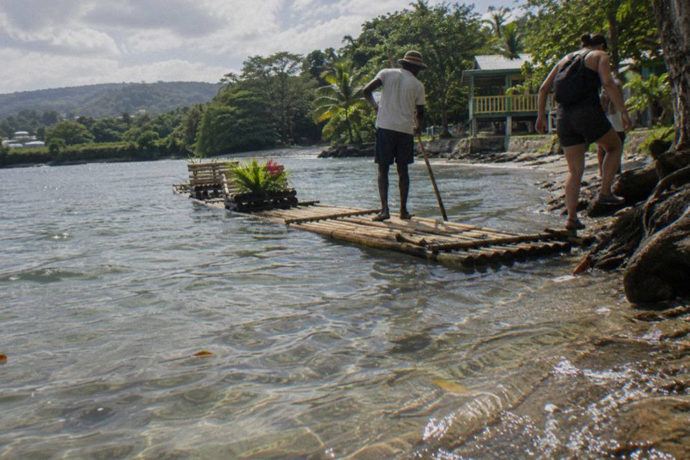 A bamboo raft resting in shallow clear water beside a green riverbank