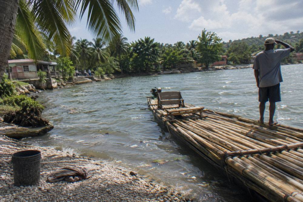 A bamboo raft resting at a riverbank landing beside calm water and overhanging trees
