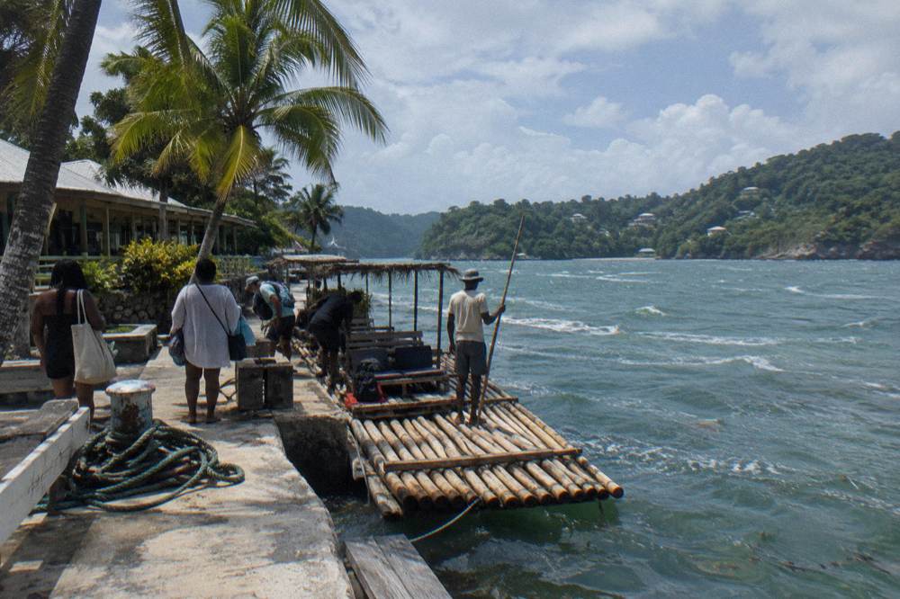 A quiet Jamaican river bend at midday with a bamboo raft visible in the distance