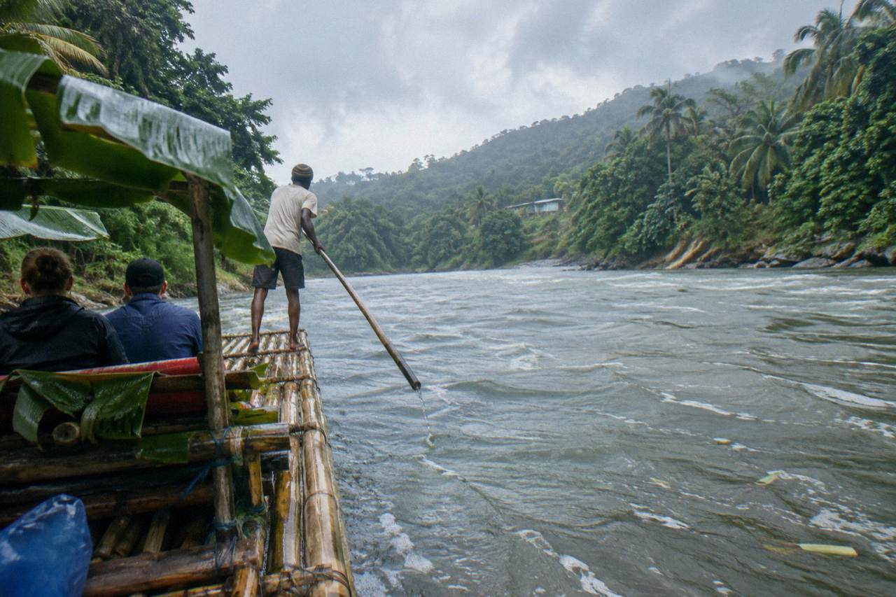 A long bamboo raft drifting on a calm green Jamaican river between tree-covered banks