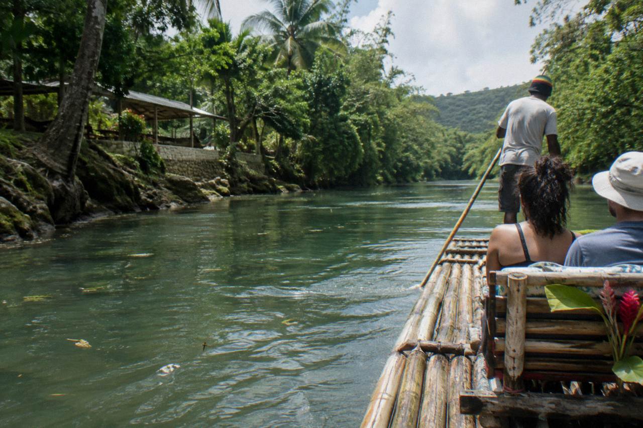 A long bamboo raft drifting on calm green river water between forested banks