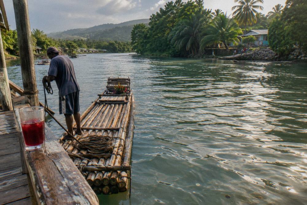 A long bamboo raft resting on still green river water beside a wooden jetty