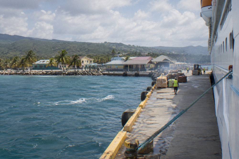 A cruise ship tied at a modern pier beside a low-rise Caribbean waterfront town