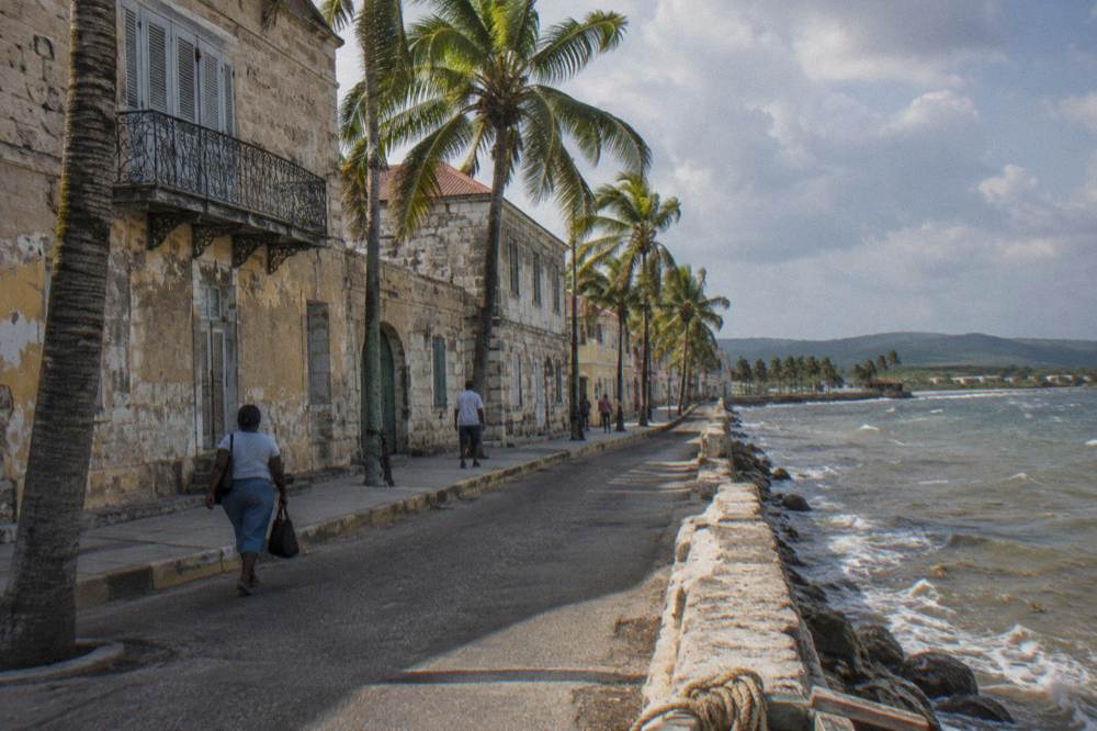 A historic seaside town street with stone buildings and palm trees