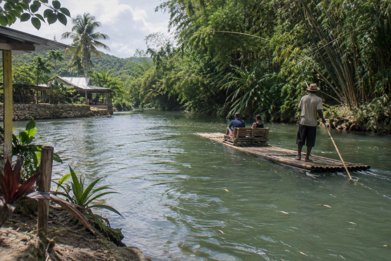 A bamboo raft drifting on a calm green river between forested banks in Jamaica