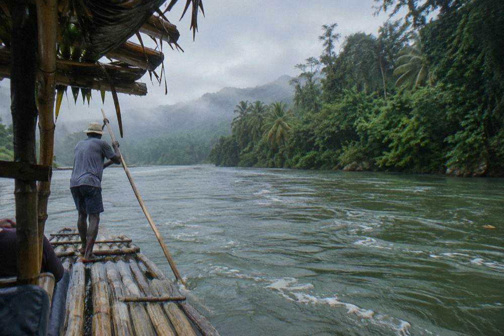 A bamboo raft floating on a wide green river between rainforest covered banks