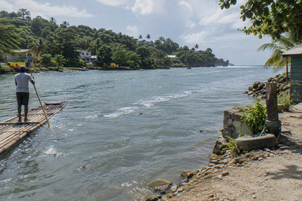 A bamboo raft crossing a calm wide river reach near Port Antonio, captain poling, green headlands on the horizon