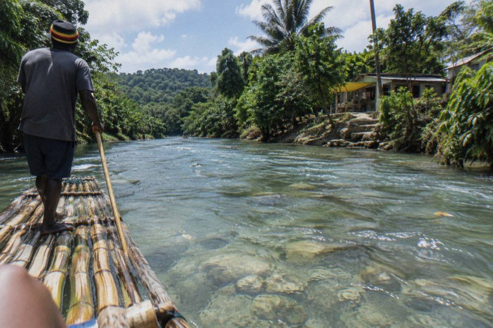 A bamboo raft gliding between dense green riverbanks under a bright sky