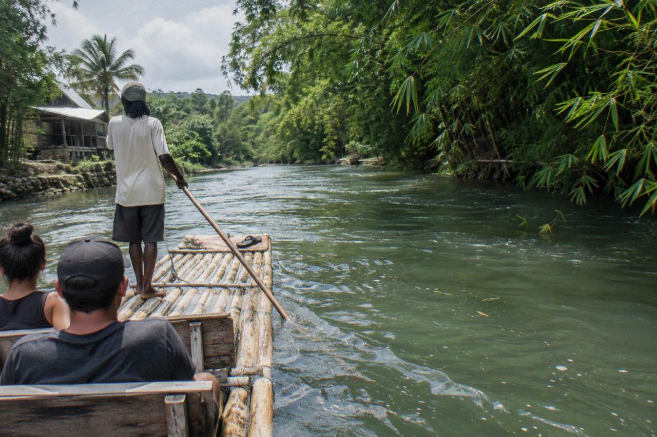 A long bamboo raft resting on calm green river water beside a forested bank in Jamaica