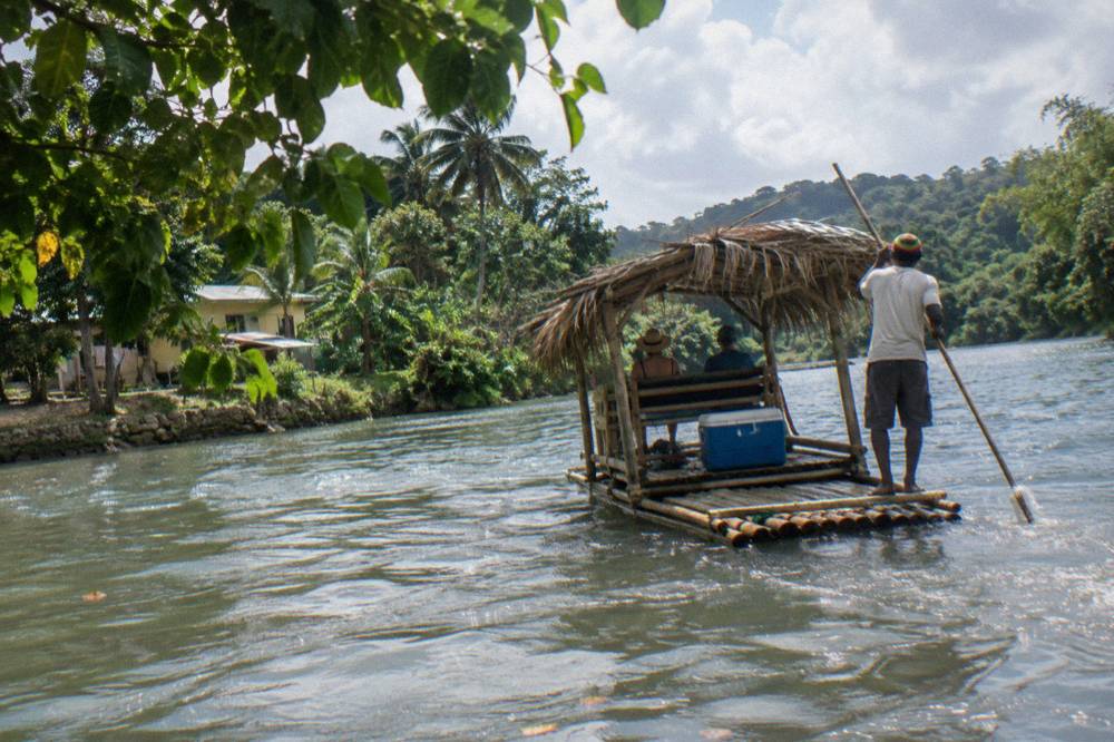A covered bamboo raft drifting past overhanging trees on a slow Jamaican river