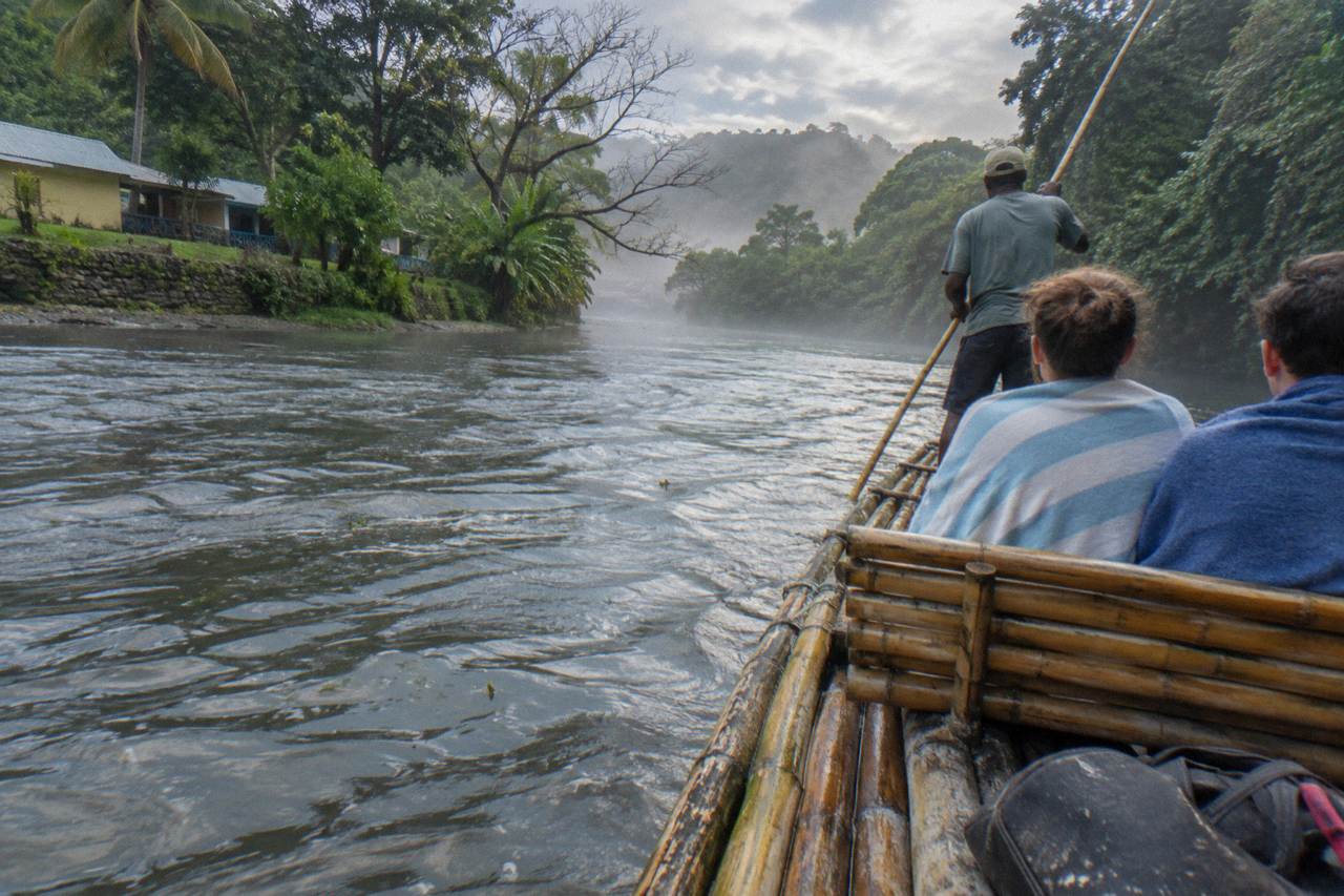 A long bamboo raft floating on a calm green river between tree-lined banks in Jamaica