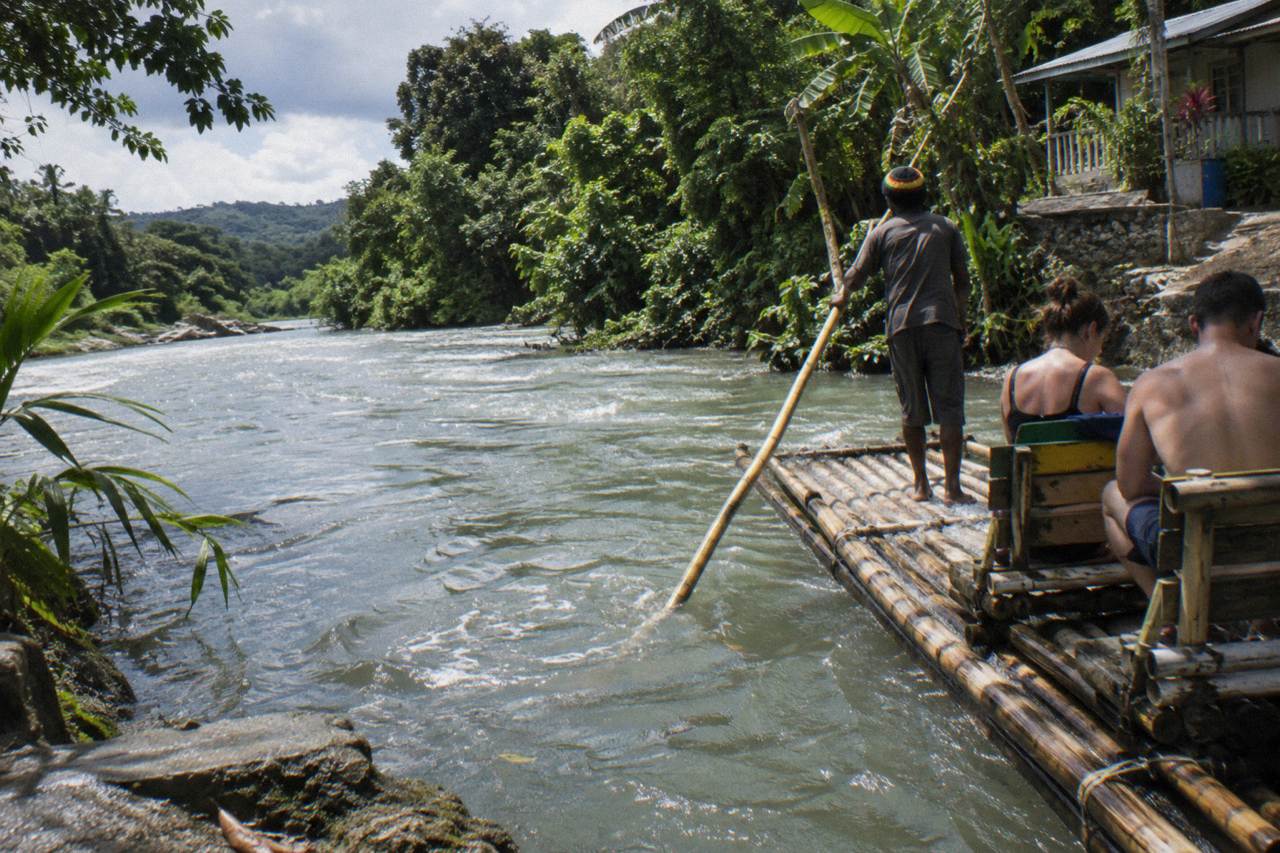 A bamboo raft resting on a calm green river beside a dense tropical riverbank