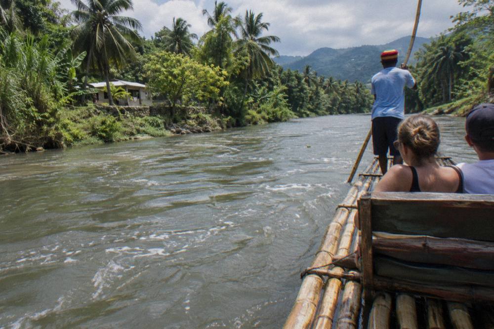 A long bamboo raft drifting on calm green water between dense tropical riverbank vegetation