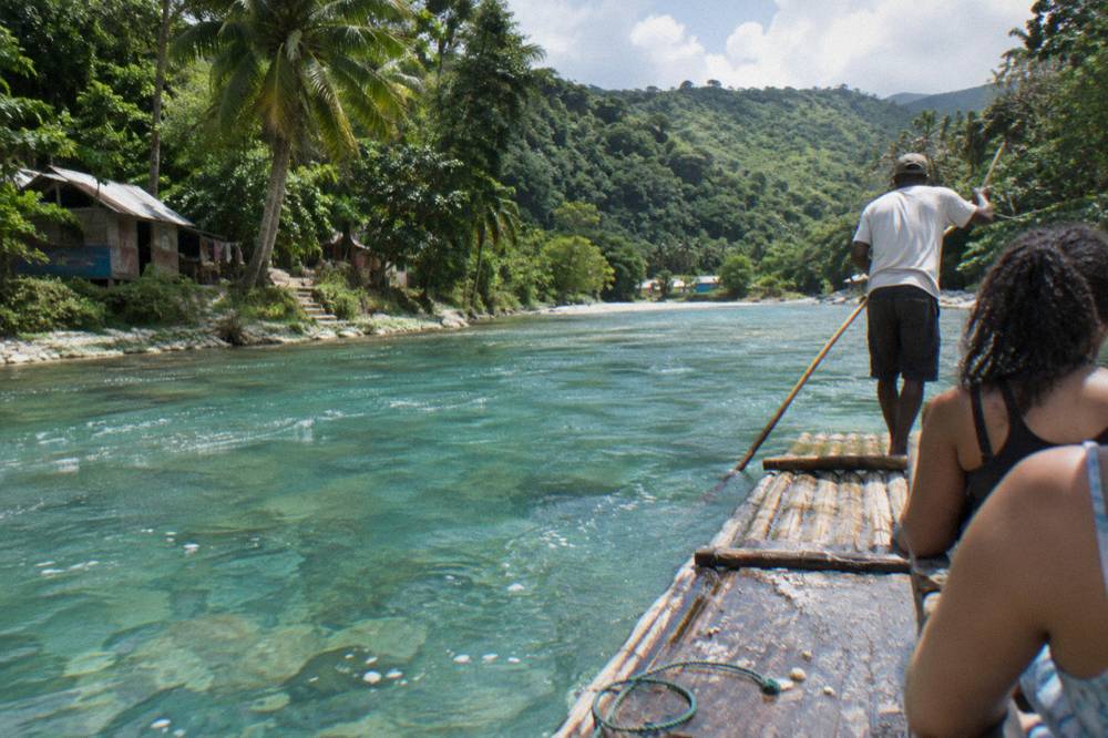 Clear turquoise river water flowing over pale stones between leafy banks in bright daylight