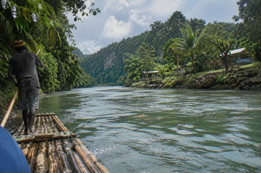 A wide tropical river valley under bright morning light with forested hills on both sides