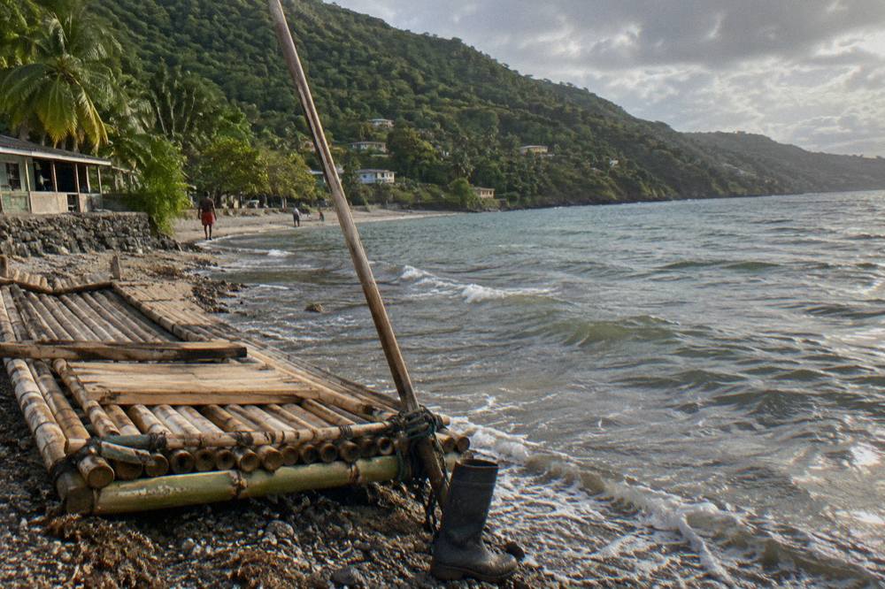 A bamboo raft resting on a riverbank with green forest slopes rising behind it