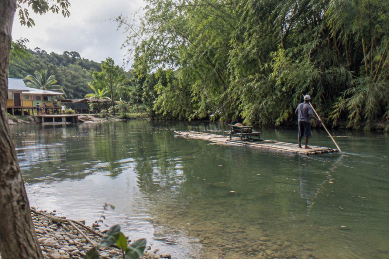 A bamboo raft drifting on a calm green river between thick tropical trees
