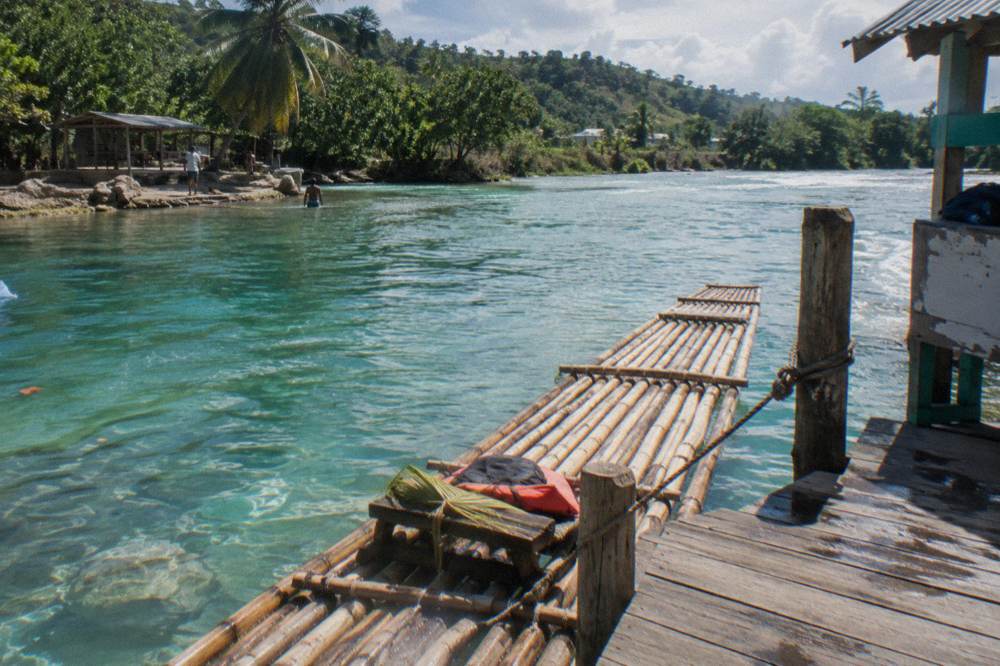 A bamboo raft tied at a small wooden jetty on a wide calm river at midday