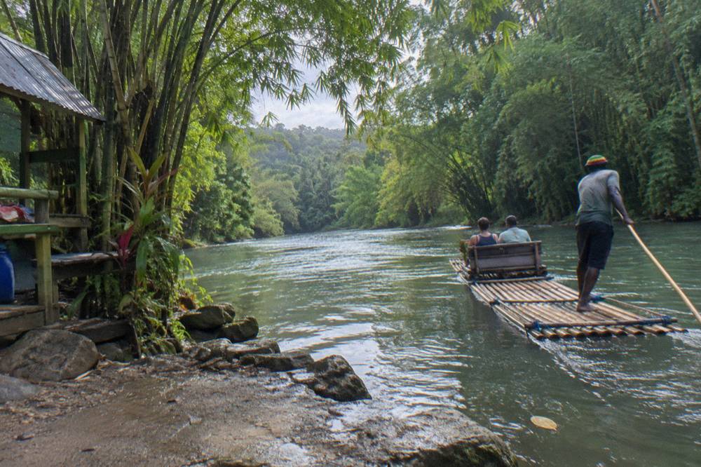A raft captain poling a bamboo raft along a calm jungle river