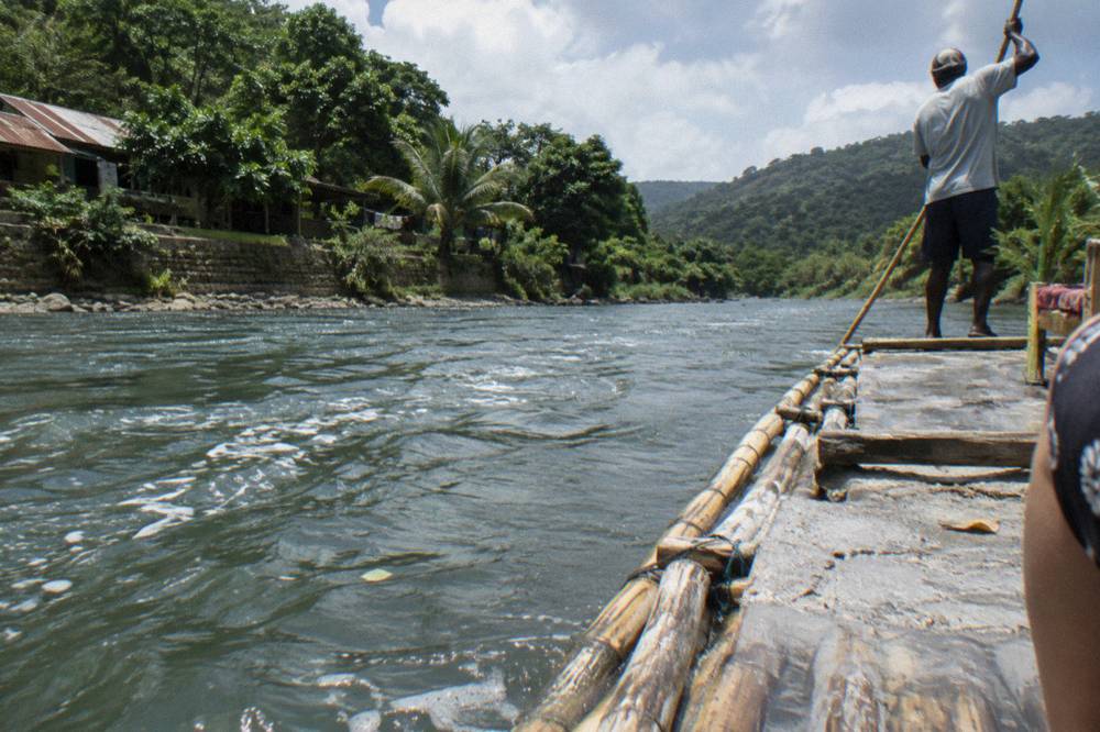 A bamboo raft midstream with a grey paste of ground limestone smeared on the deck and the captain standing aft with his pole raised