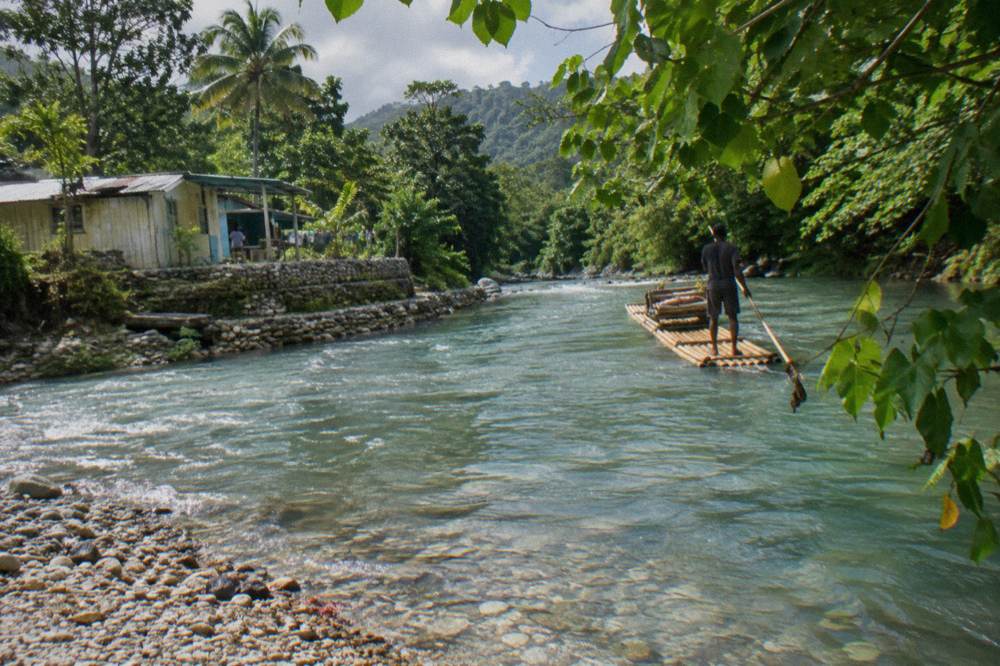 A bamboo raft gliding between overhanging green branches on a narrow calm river