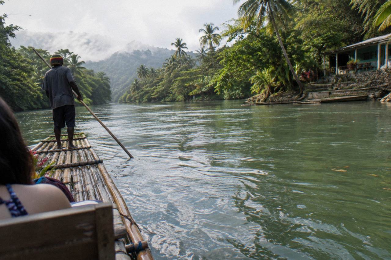 A long bamboo raft drifting on calm green river water between tree-lined banks