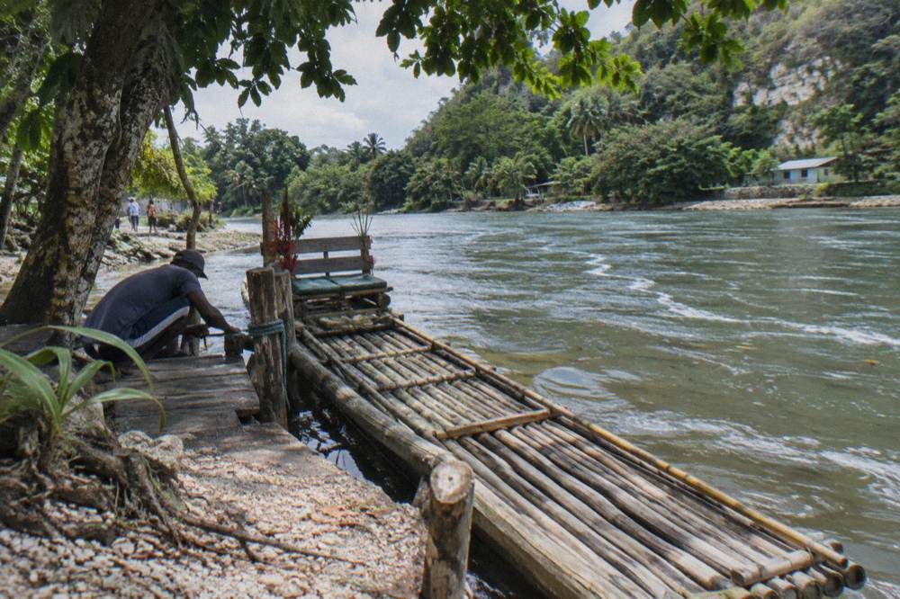 A bamboo raft resting at a small wooden river dock under overhanging trees
