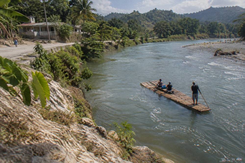 A wide slow river bend reflecting green hills under a bright sky