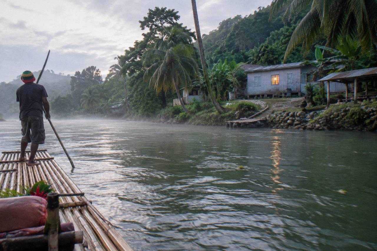 A long bamboo raft drifting on a calm green Jamaican river between forested banks