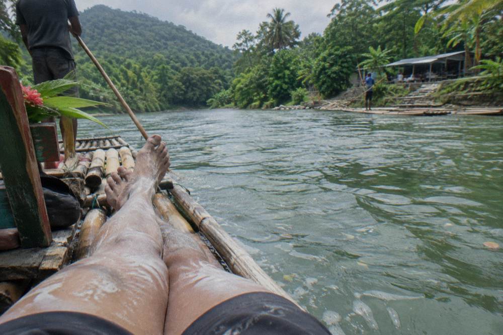 Pale limestone paste drying on a passenger's legs as a bamboo raft glides through calm green water