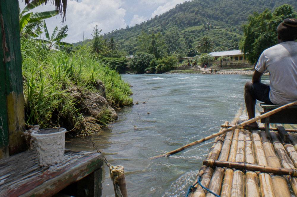 A bamboo raft moored at a grassy riverbank with dense green hills rising behind it