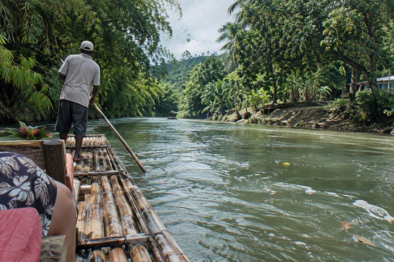 A bamboo raft drifting on a calm green river with rainforest banks under a bright sky