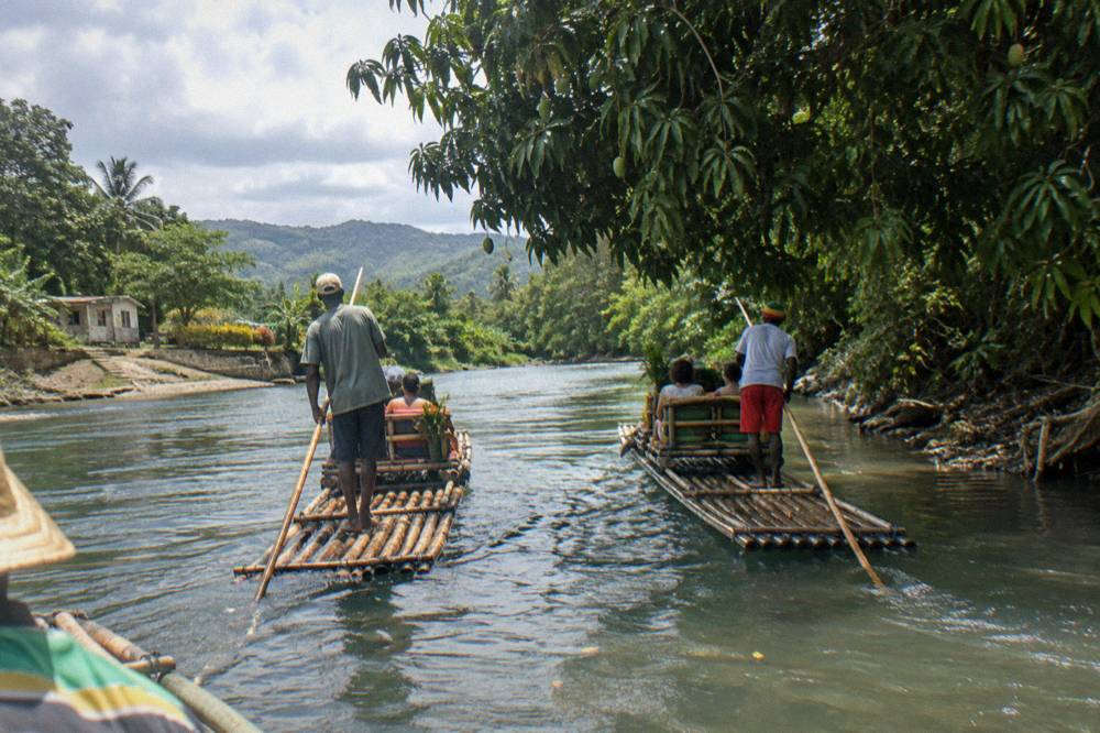 Two bamboo rafts floating side by side on a slow green river beneath overhanging trees