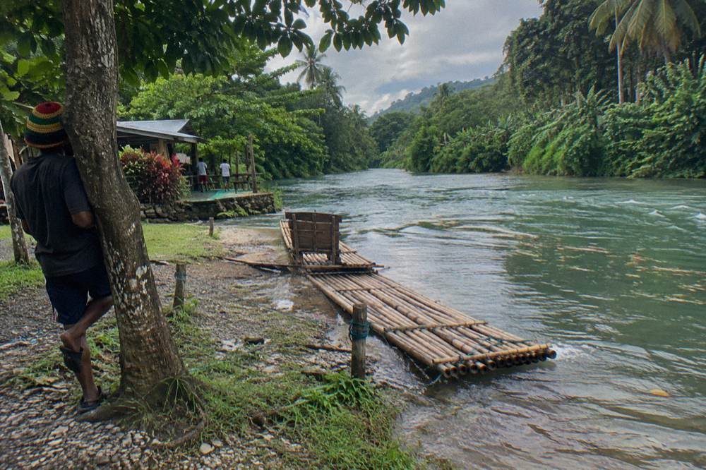 A quiet riverbank landing spot with a bamboo raft tied at the edge of calm shallow water