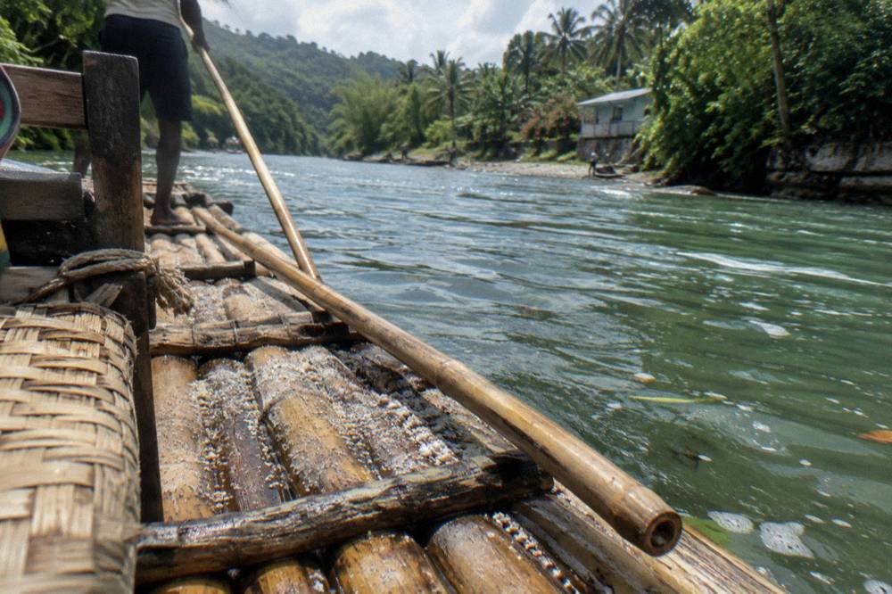 A close view of a bamboo raft seat and a captain's pole resting beside green water