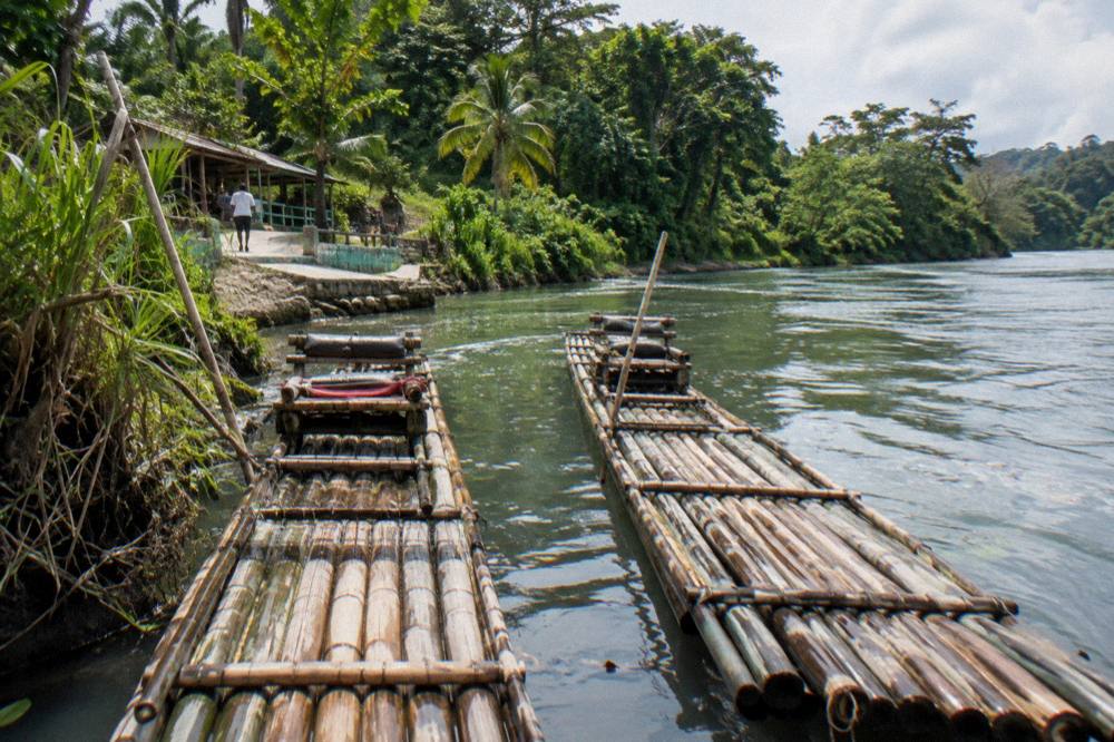 Two bamboo rafts moored at a quiet river landing with dense green forest behind