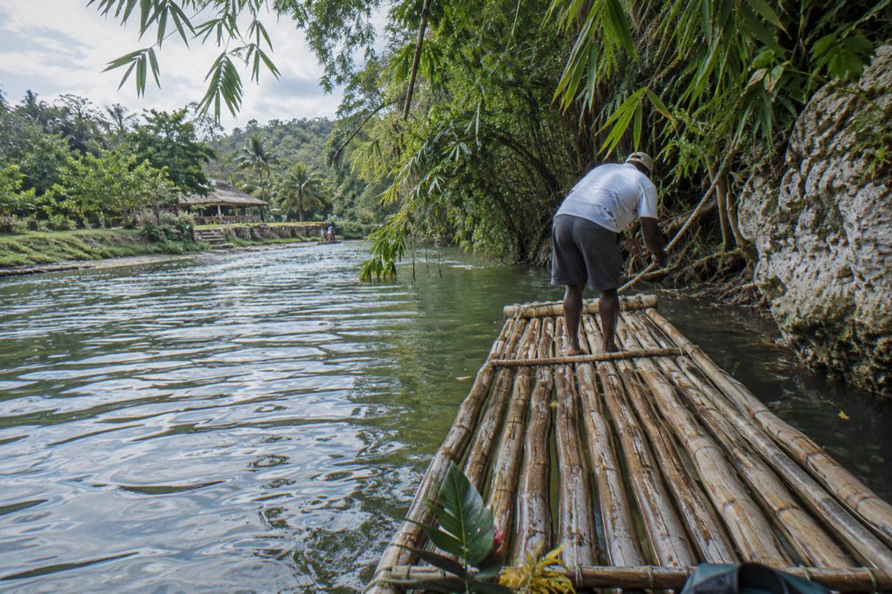 A bamboo raft resting on a calm green Jamaican river beside overhanging trees