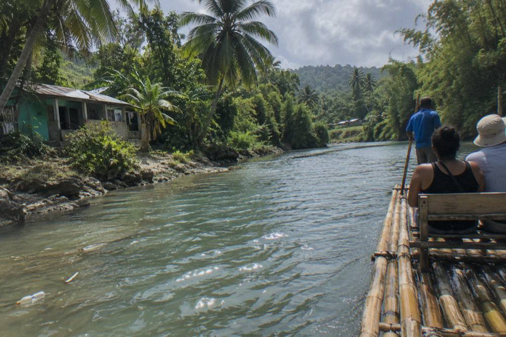 A long bamboo raft floating on calm river water between green riverbanks