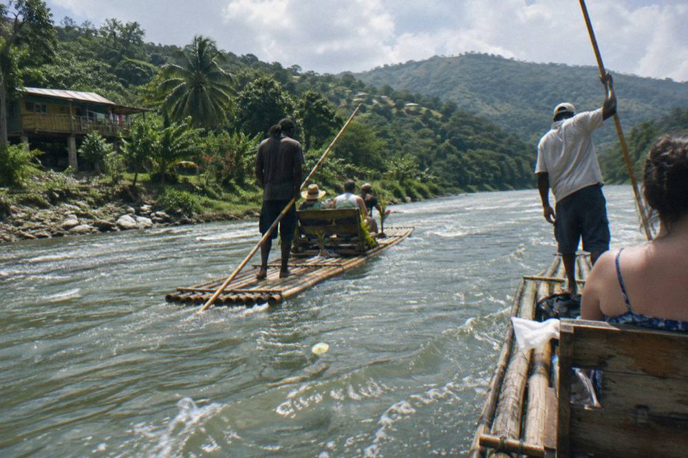Two bamboo rafts drifting side by side on a slow river between green hills
