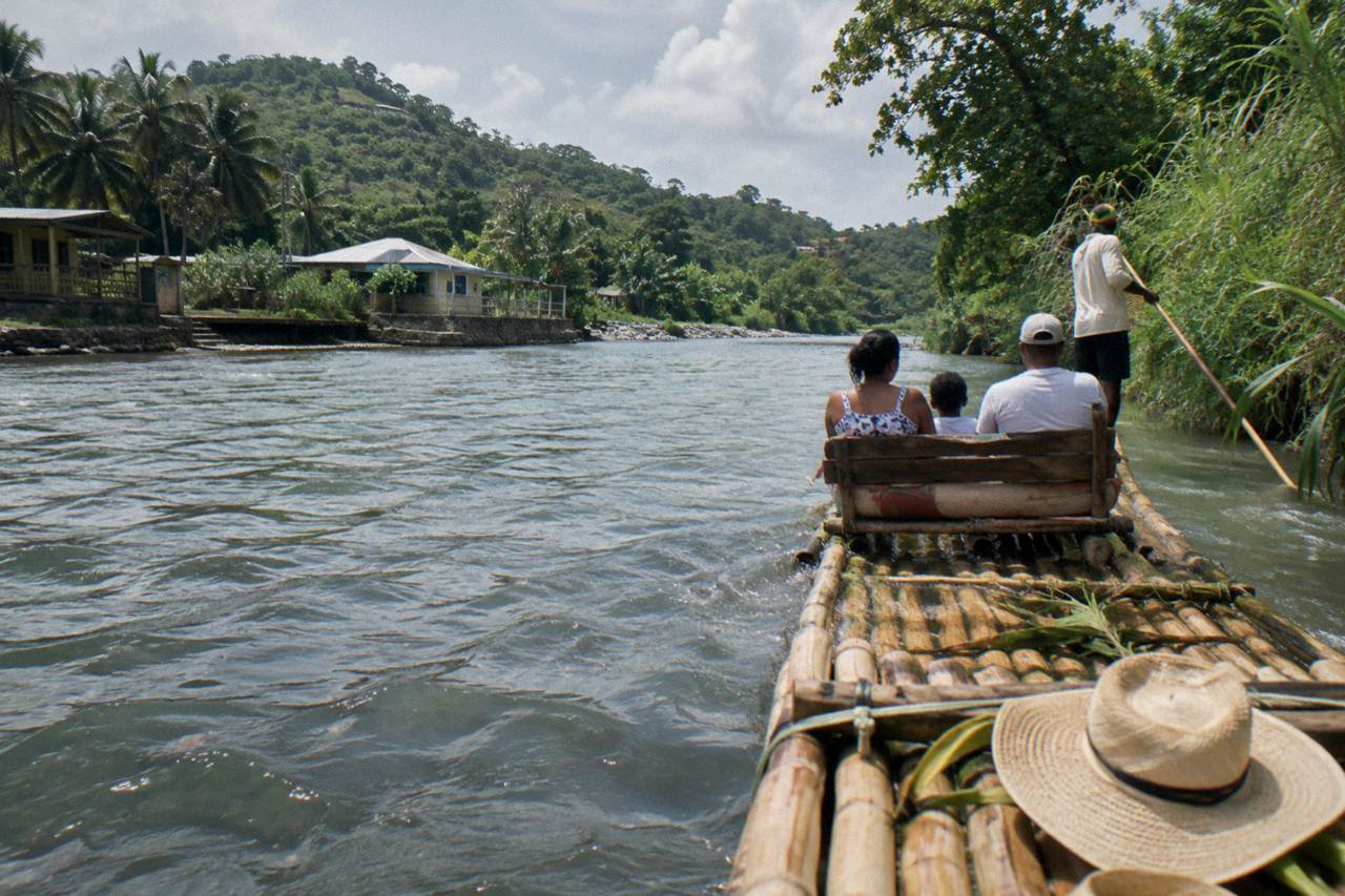 A bamboo raft resting on a calm green Jamaican river beside a grassy bank