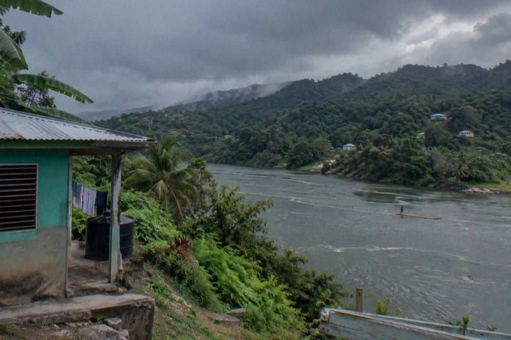 Dark rain clouds gathering over green Jamaican hills above a river valley
