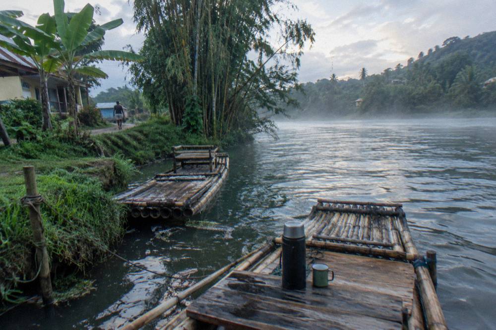 Early morning light on a calm river with mist over the water and bamboo rafts moored at the bank