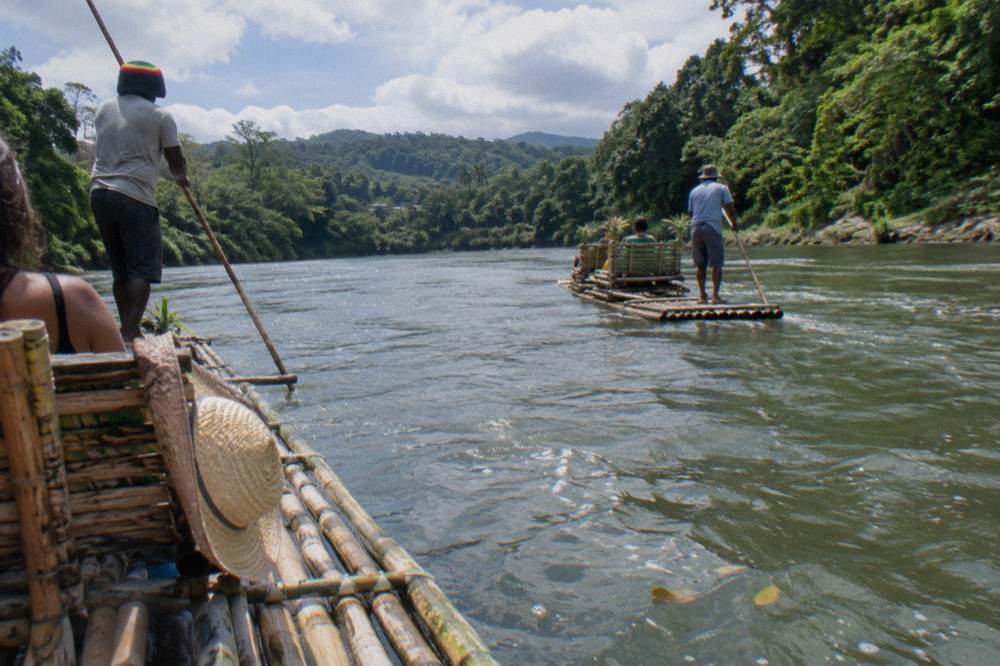 Two bamboo rafts on a wide river surrounded by dense green forest on both banks