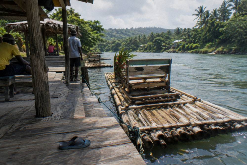 A quiet rafting departure point on a riverbank with a bamboo raft tied at a wooden dock