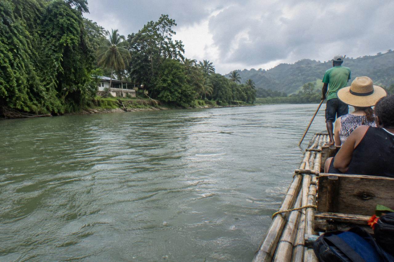 A bamboo raft drifting on a calm green Jamaican river between tree-lined banks