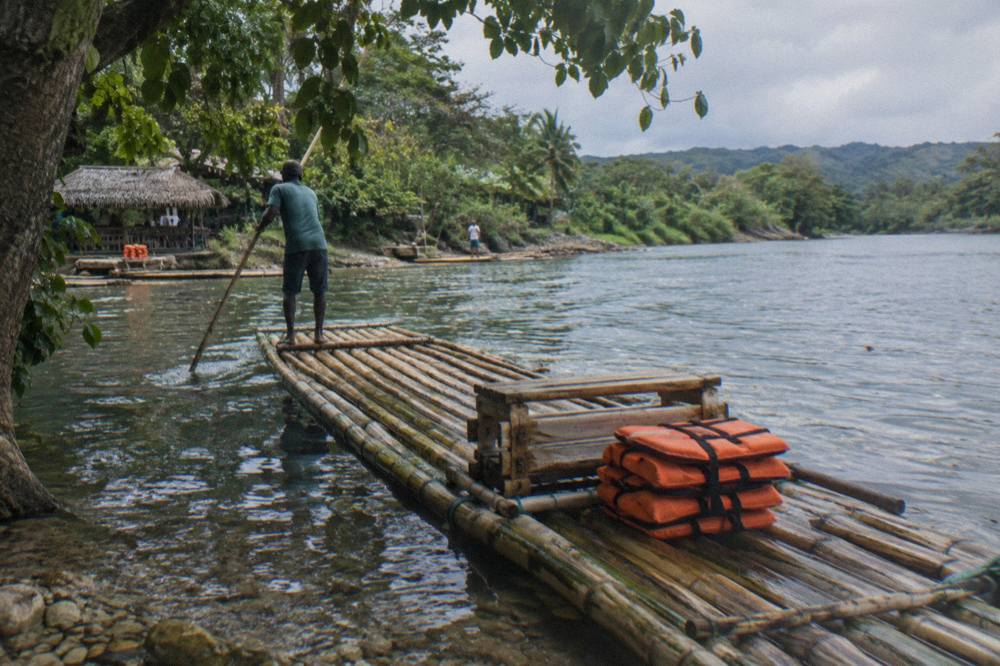 A bamboo raft resting at a riverbank landing beside overhanging trees on still water