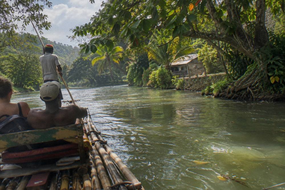 A bamboo raft drifting on calm green water between tree-lined banks